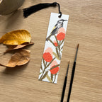 Bookmark with bird and floral design on a wooden surface with leaves and paintbrushes.