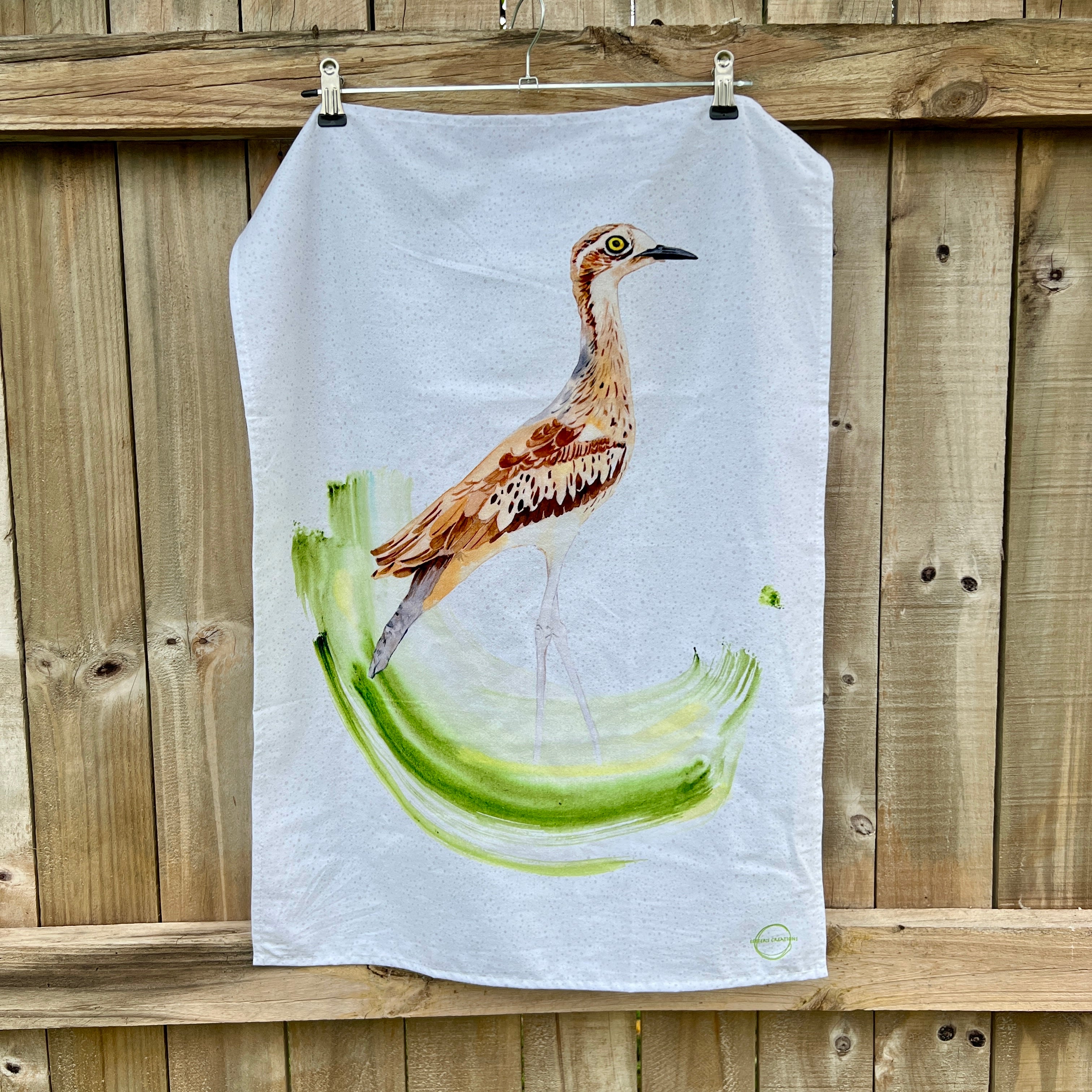 Tea towel with a curlew bird design hanging on a wooden fence