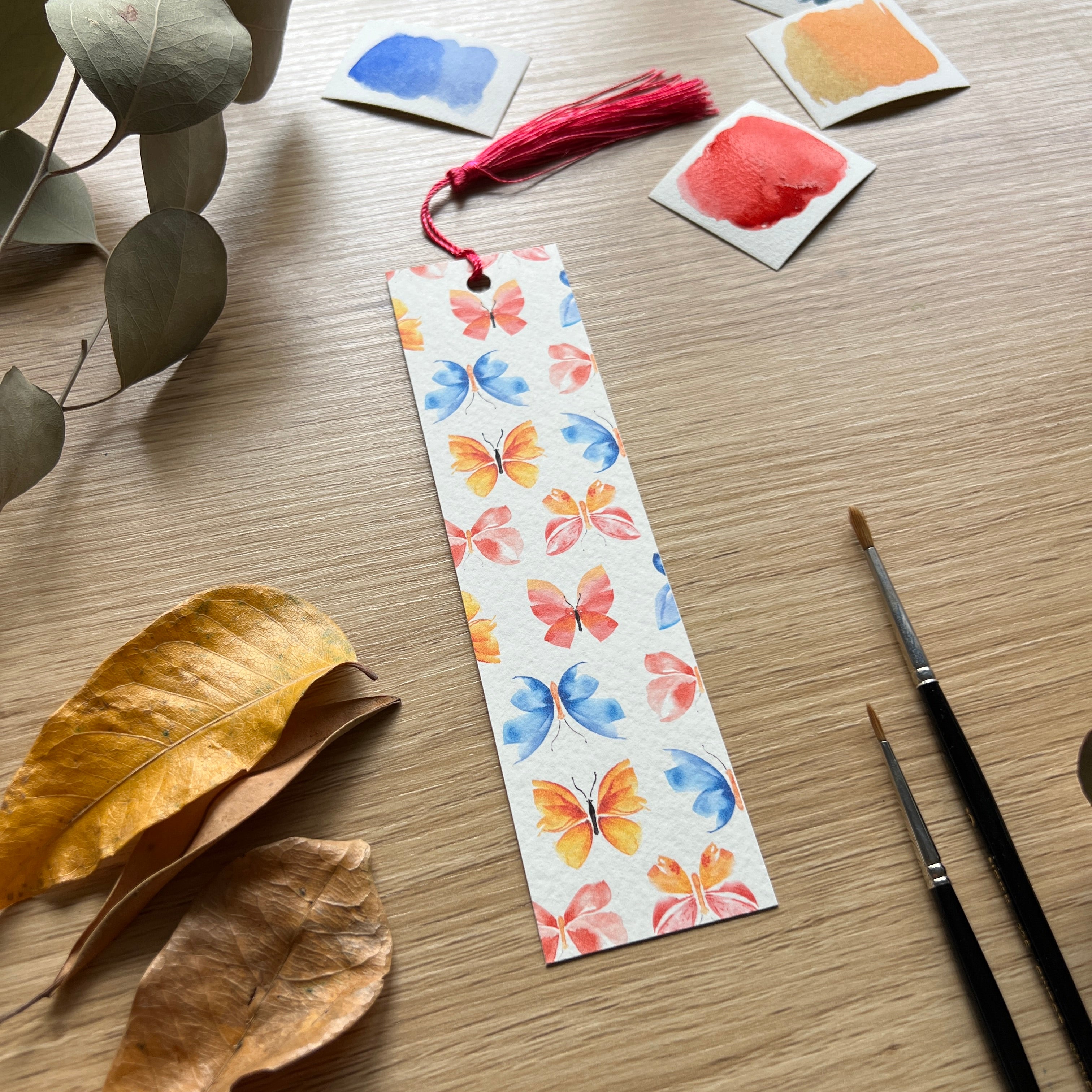 Colorful butterfly bookmark on a wooden surface with paint samples and brushes.