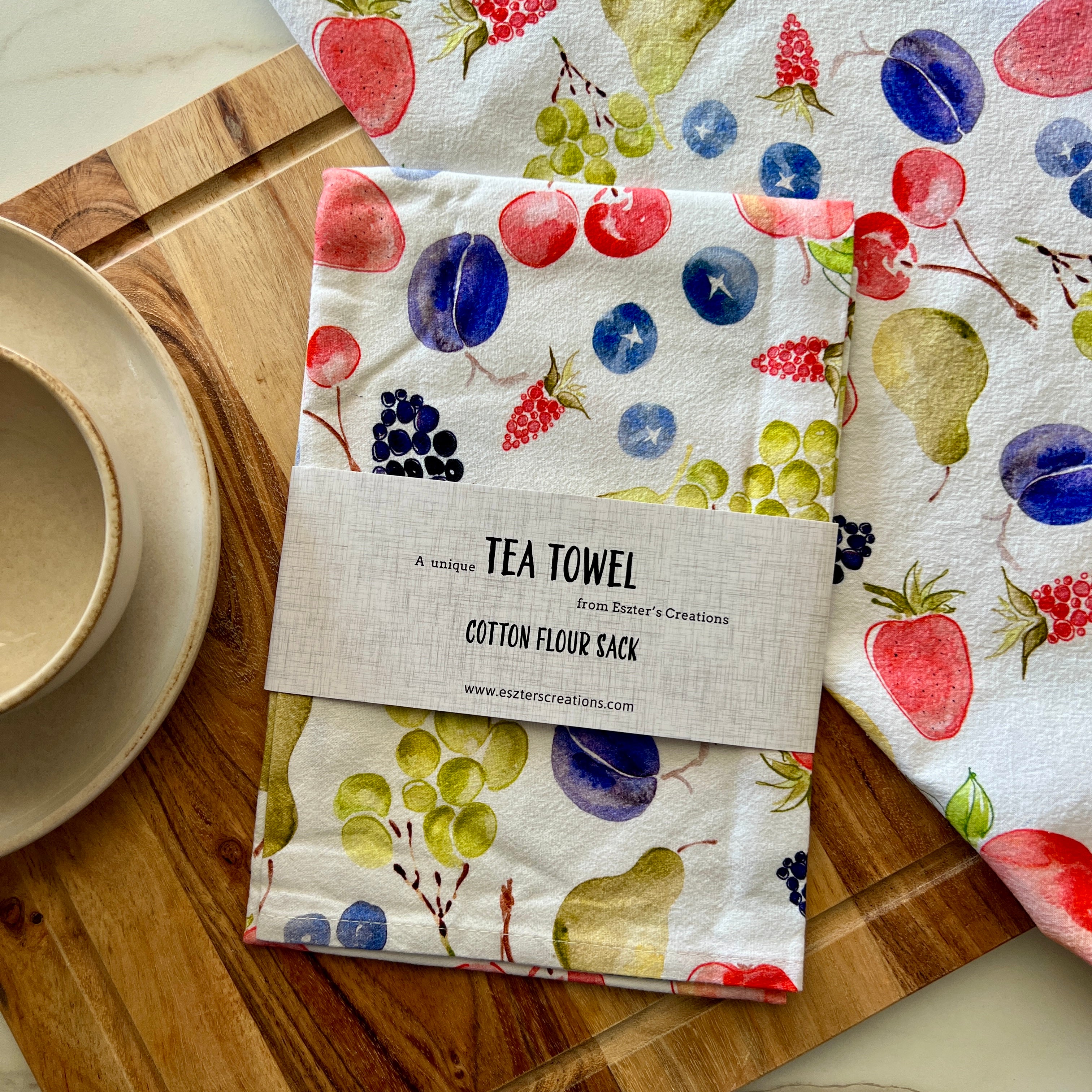Tea towel with fruit pattern such as cherries, berries, pear and plum on a wooden kitchen chopping board