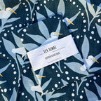 Tea towel with bird and leaf pattern and label on a dark blue background