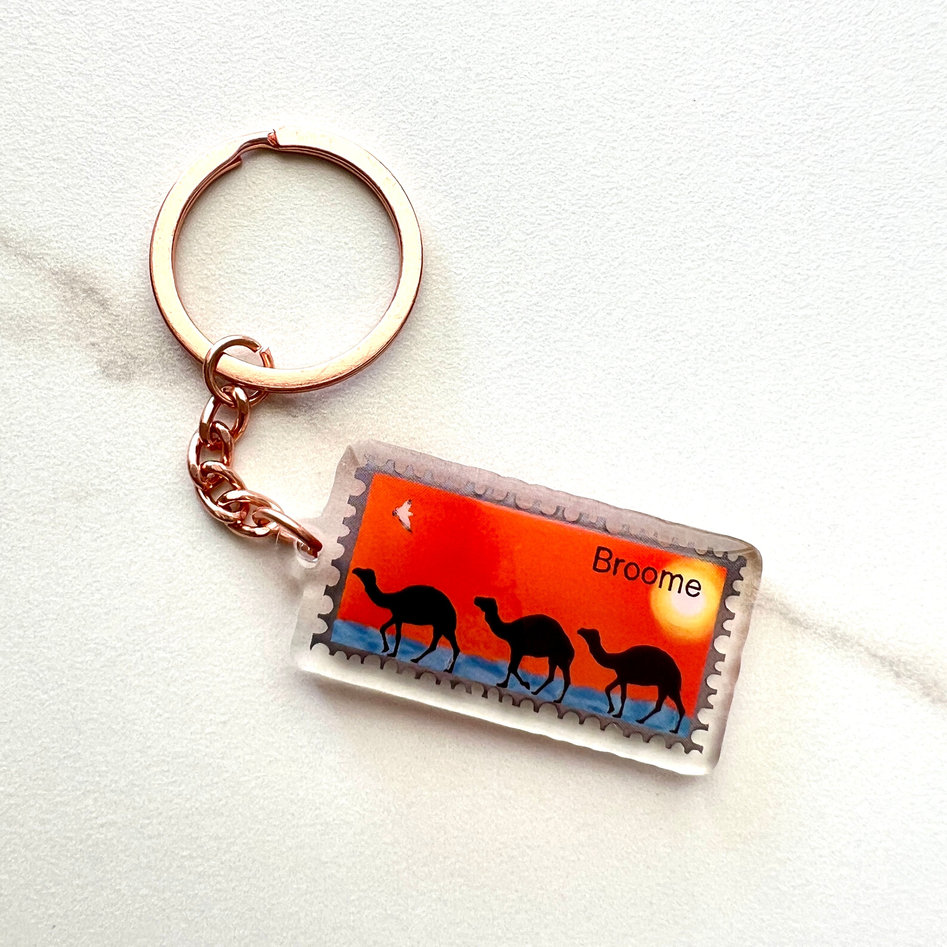 Broome-themed acrylic keychain featuring three illustrated camels on a vibrant orange background, ideal Australian souvenir or travel gift.