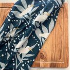 Navy blue cotton tea towel with white egret bird pattern on a wooden surface