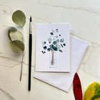 Greeting card with eucalyptus design on a marble surface with leaves and a pen.