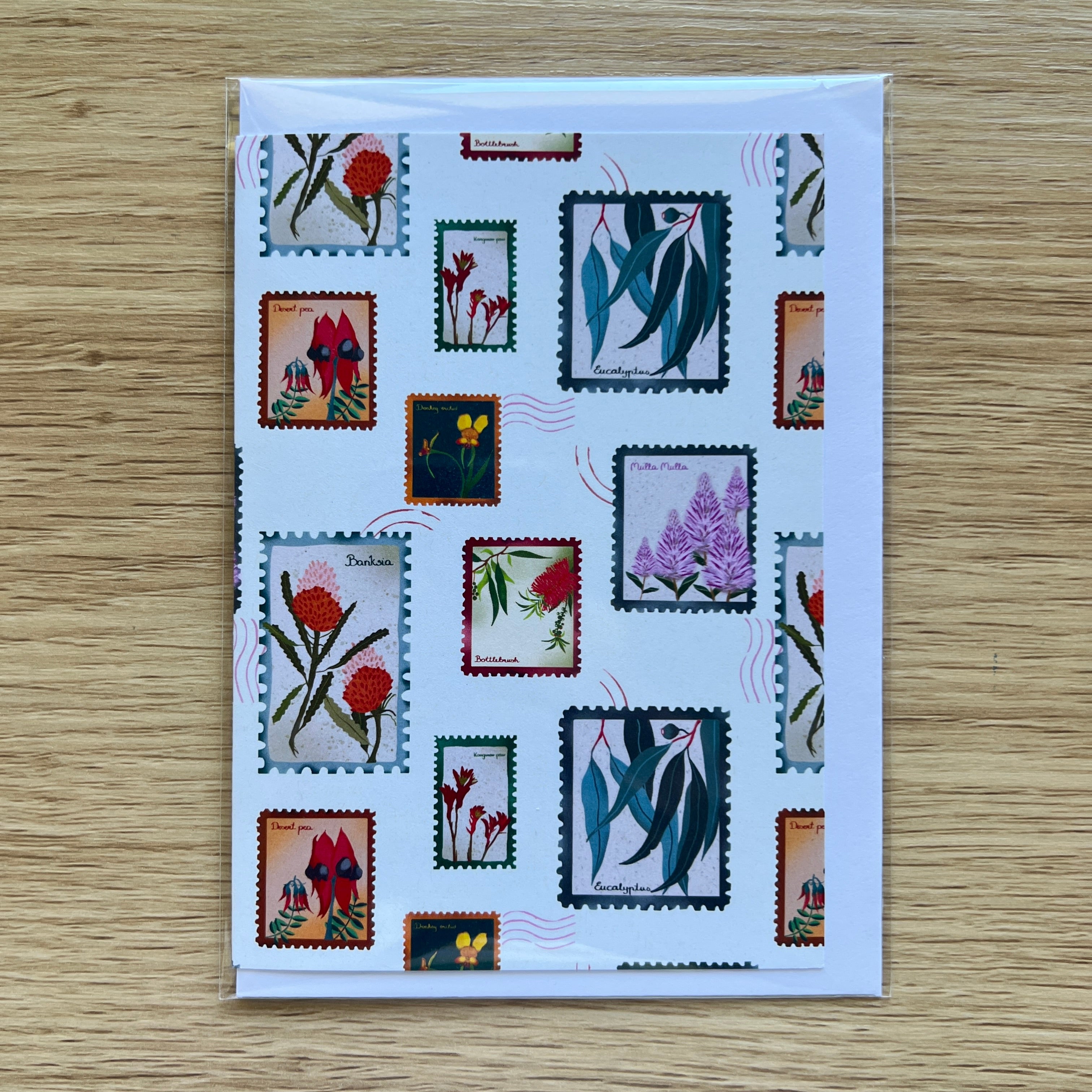Card with postage stamp designs featuring floral and nature-themed illustrations on a wooden surface.