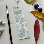 Bookmark with eucalyptus leaf design on a surface with leaves and paintbrush