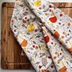 Two patterned teatowels with birds and fruits on a wooden surface