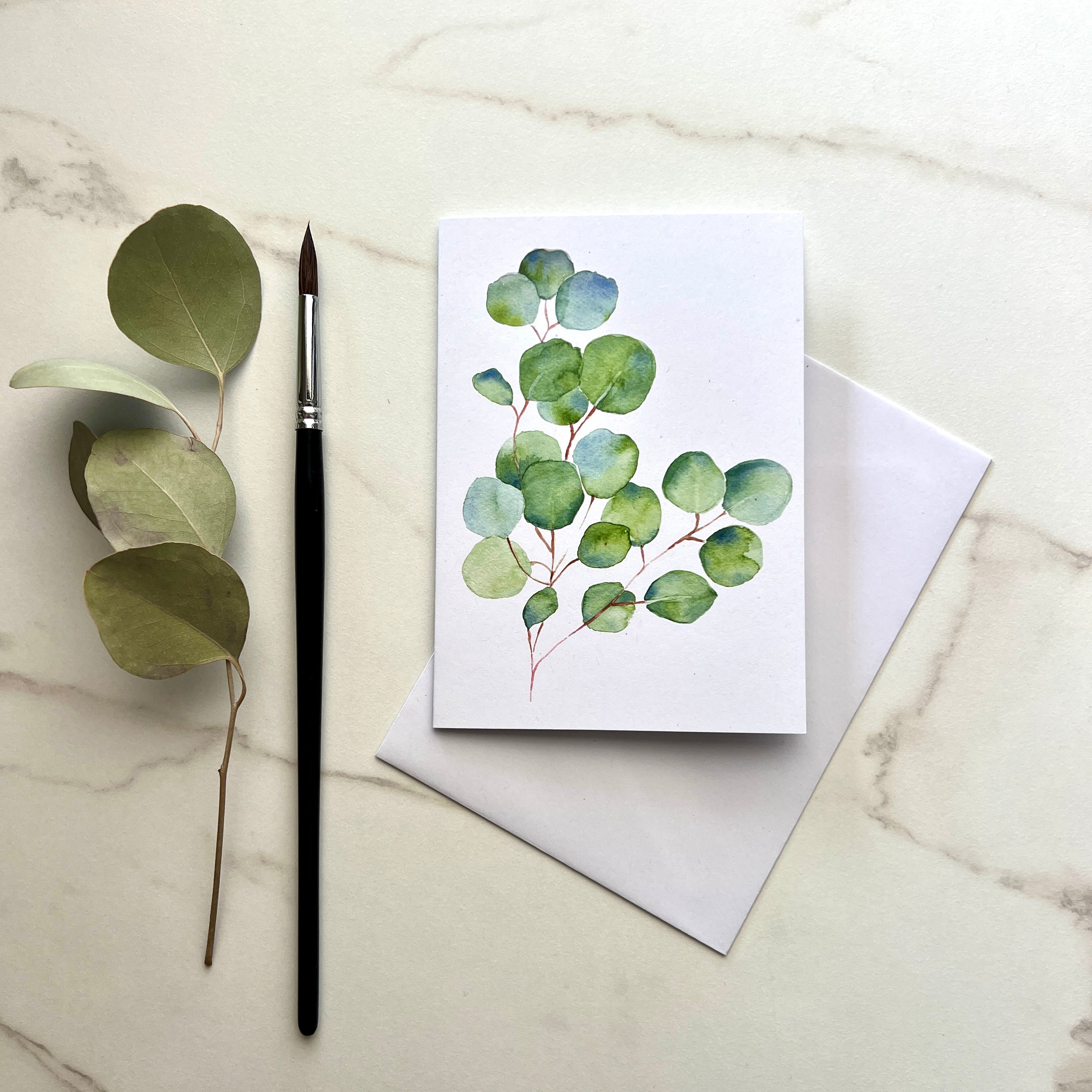 Greeting card with eucalyptus design, brush, and eucalyptus branch on marble surface