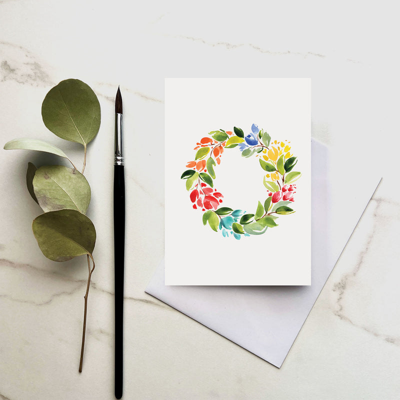 Greeting card with floral wreath design, brush, and leaves on a marble surface