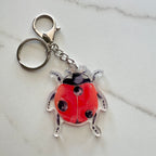 Red ladybug keychain on a light gray marble background