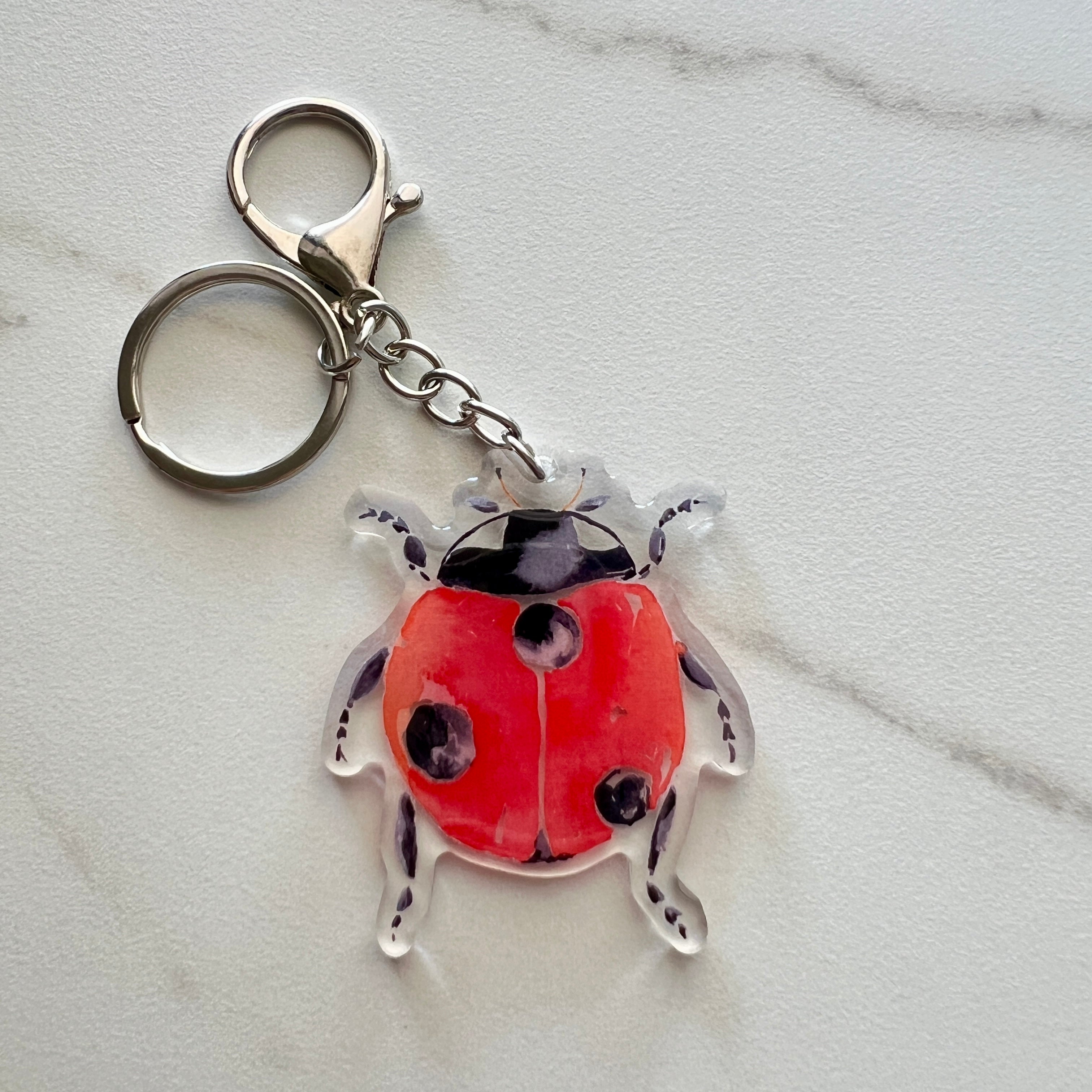 Red ladybug keychain on a light gray marble background