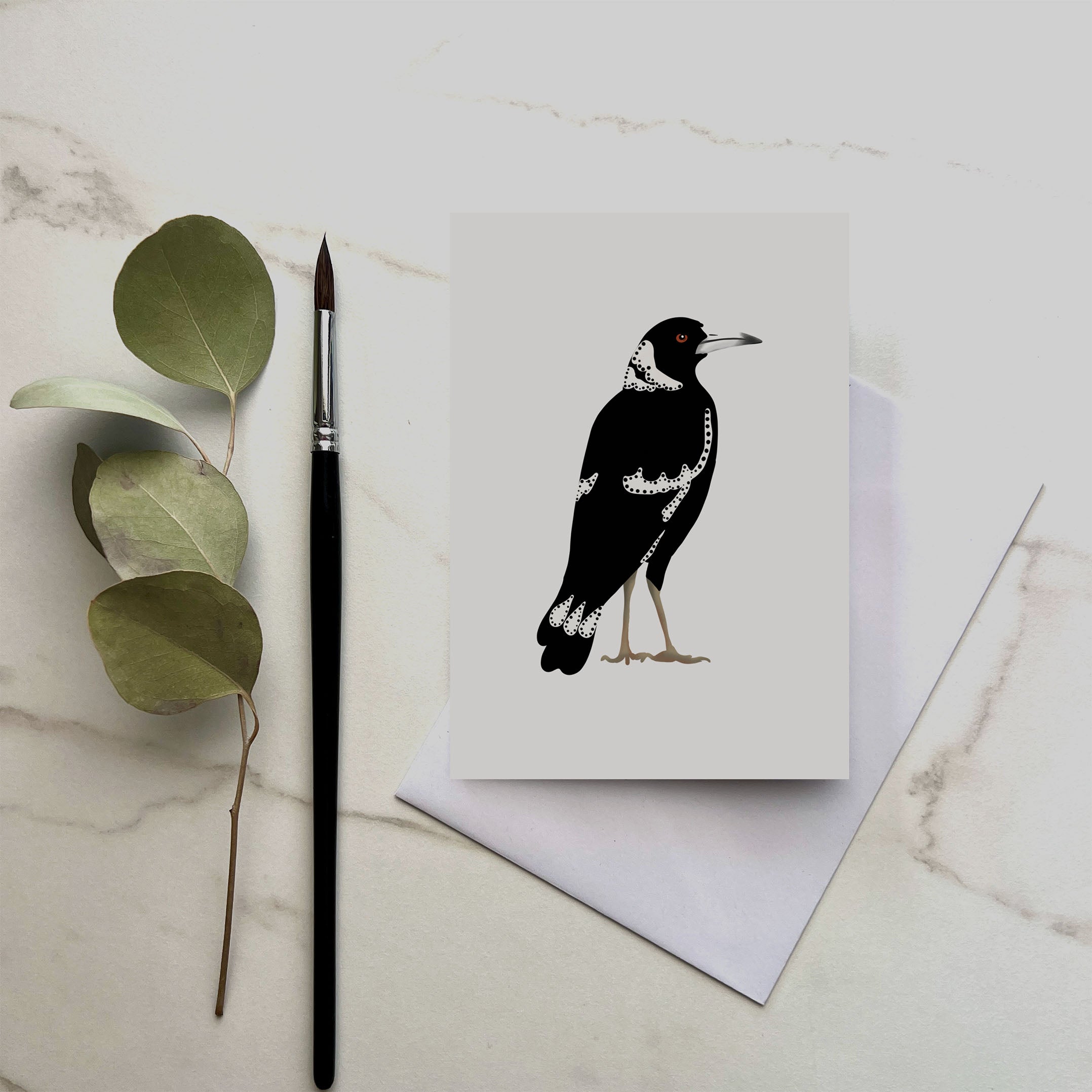 Greeting card with a black and white bird illustration on a marble surface with a brush and leaves.