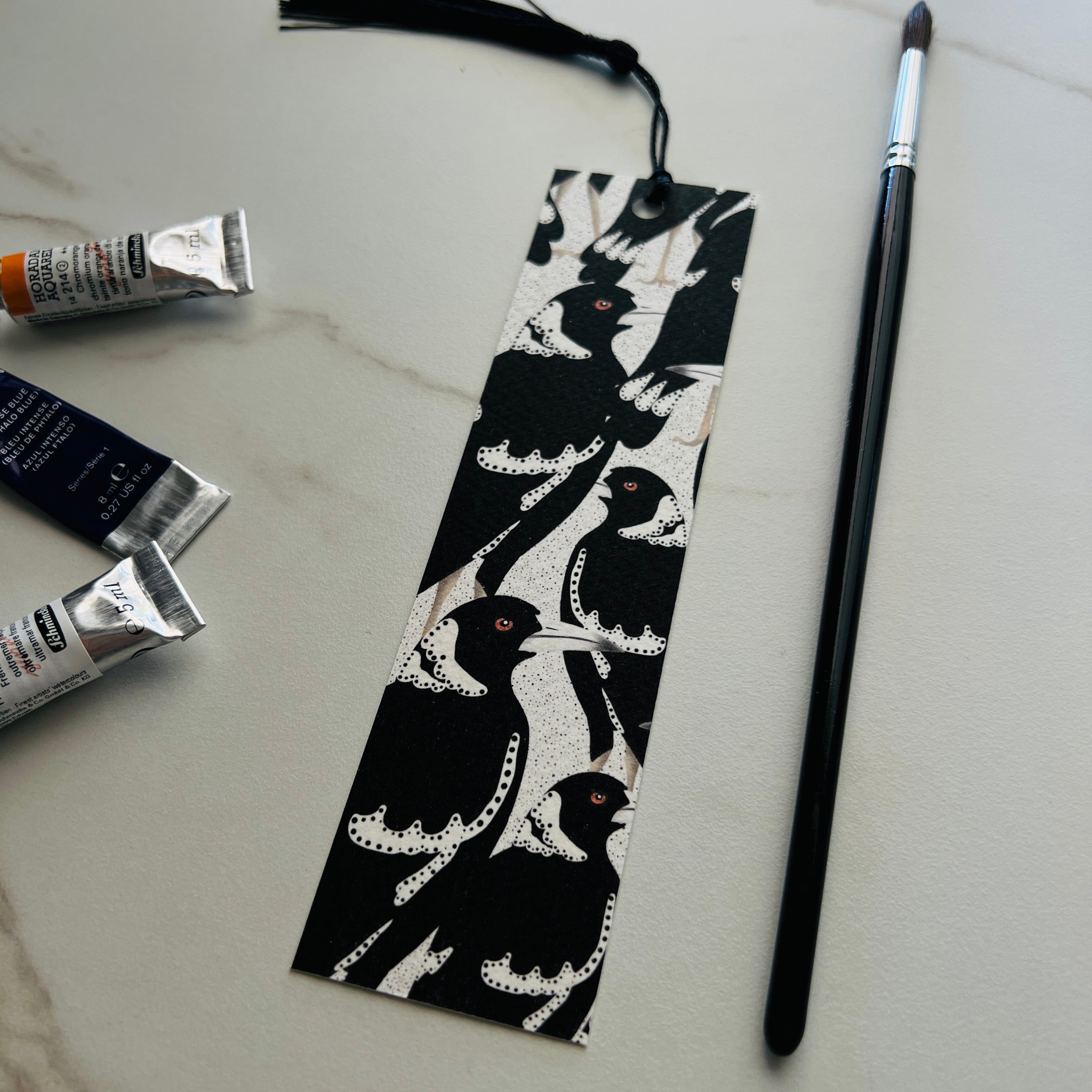 Black and white patterned  magpie bird bookmark with paint tubes and a brush on a light surface