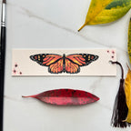 Bookmark with monarch butterfly design on a marble surface with leaves and a brush