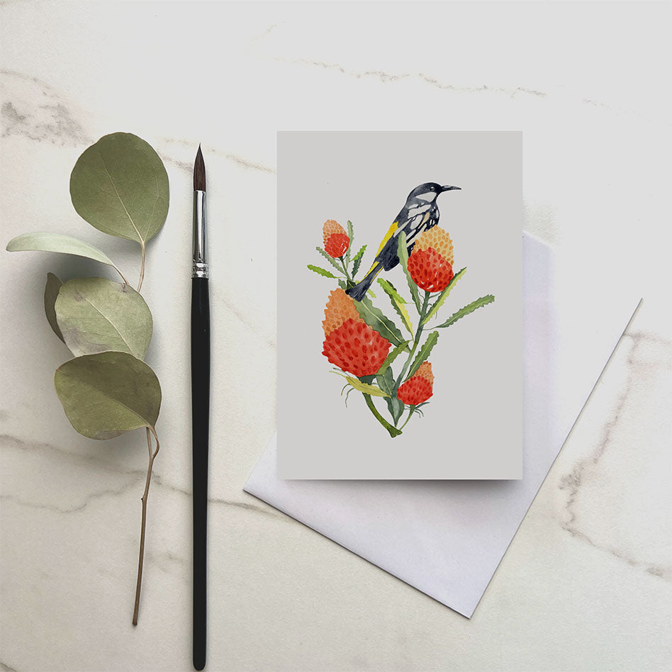Greeting card with a bird and flowers design on a marble surface with a brush and leaves.