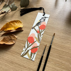 Bookmark with floral design and new holland honey eater  illustration on a wooden surface with leaves and paintbrushes.