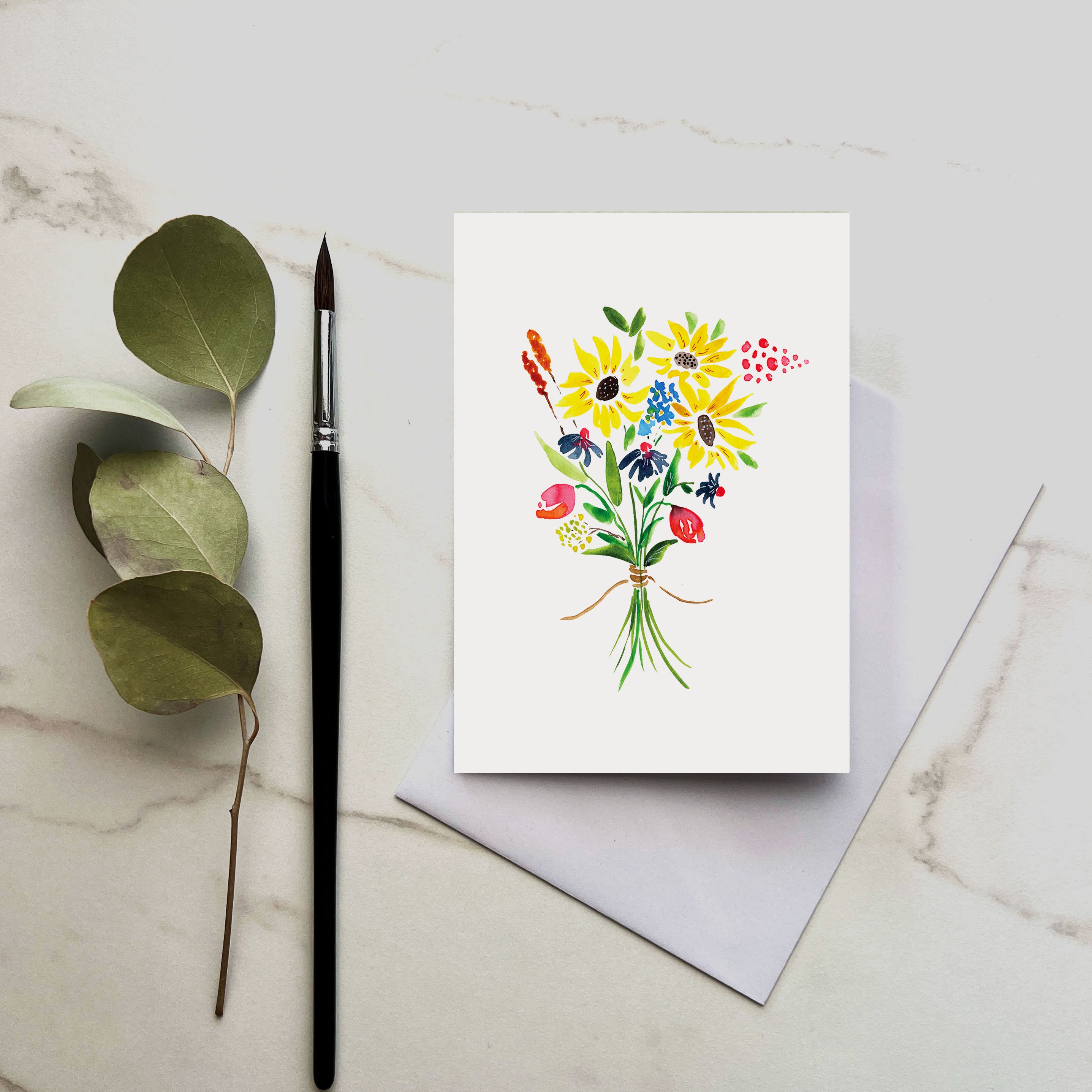 Greeting card with floral design on a marble surface with a brush and leaves.