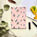 Notebook with a cockatoo and leaf pattern on a light surface with leaves and a pen.