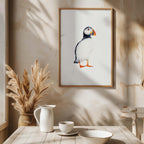 Framed artwork of a puffin on a wall above a table with decor items.