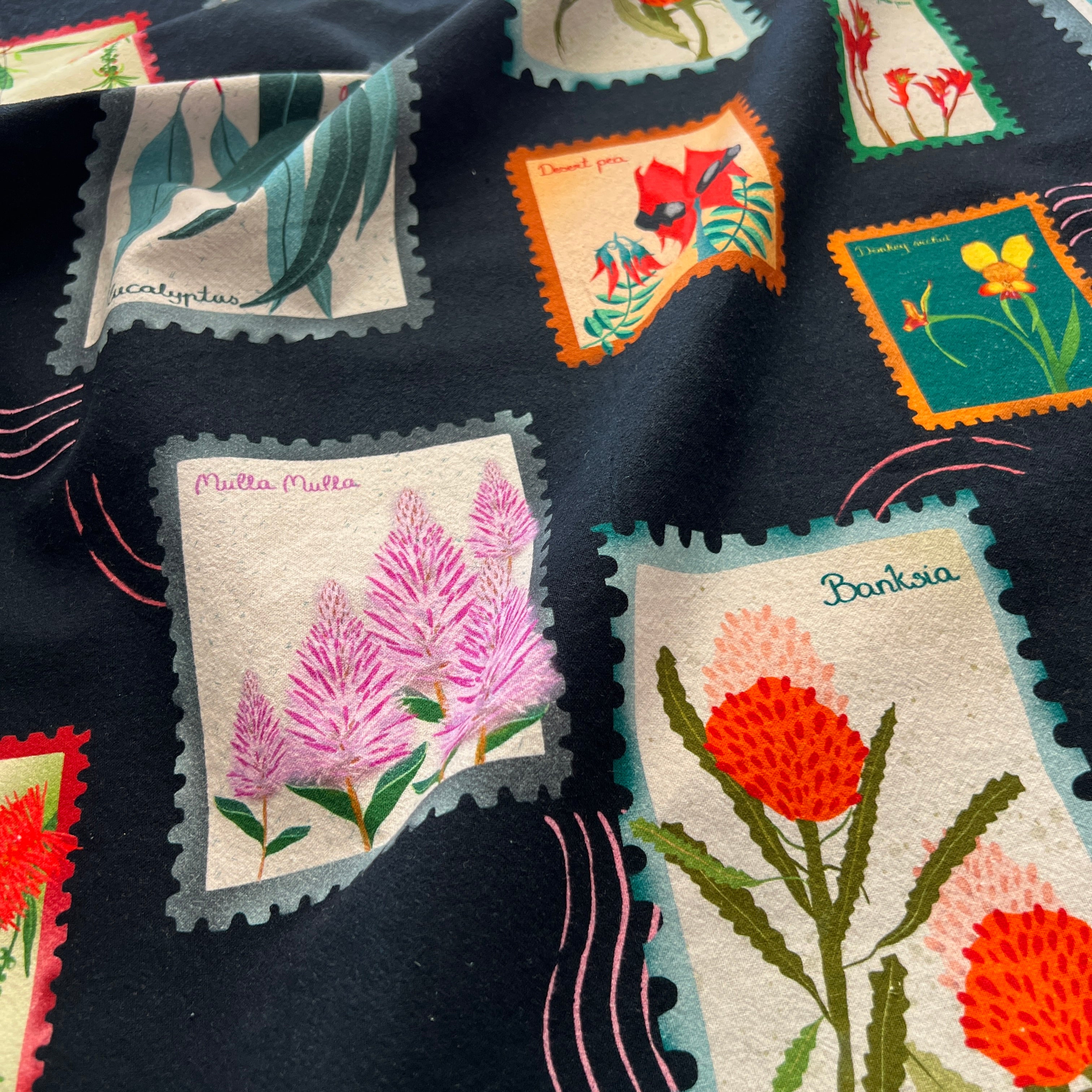 vibrant Australian wildflower stamp tea towel on black background, cotton flour sack kitchen towel by Eszter Torok