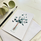Greeting card with eucalyptus design on a white surface with a paintbrush and leaves.
