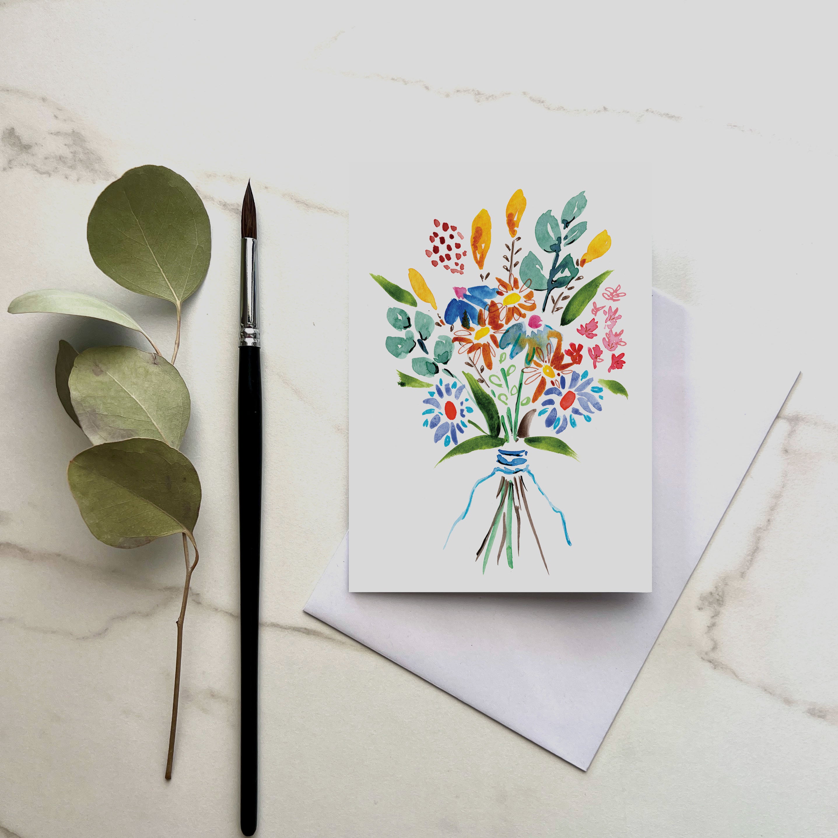 Greeting card with watercolor floral design, brush, and leaves on a marble surface