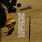 Bookmark with watercolour sea shell design on a wooden surface with leaves and a paint brush.